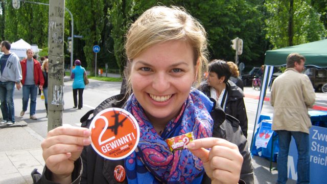 Katharina Schulze wirbt mit Flyern, Aufklebern und Nimm-Zwei-Bonbons für zwei statt drei Startbahnen am Münchner Flughafen.